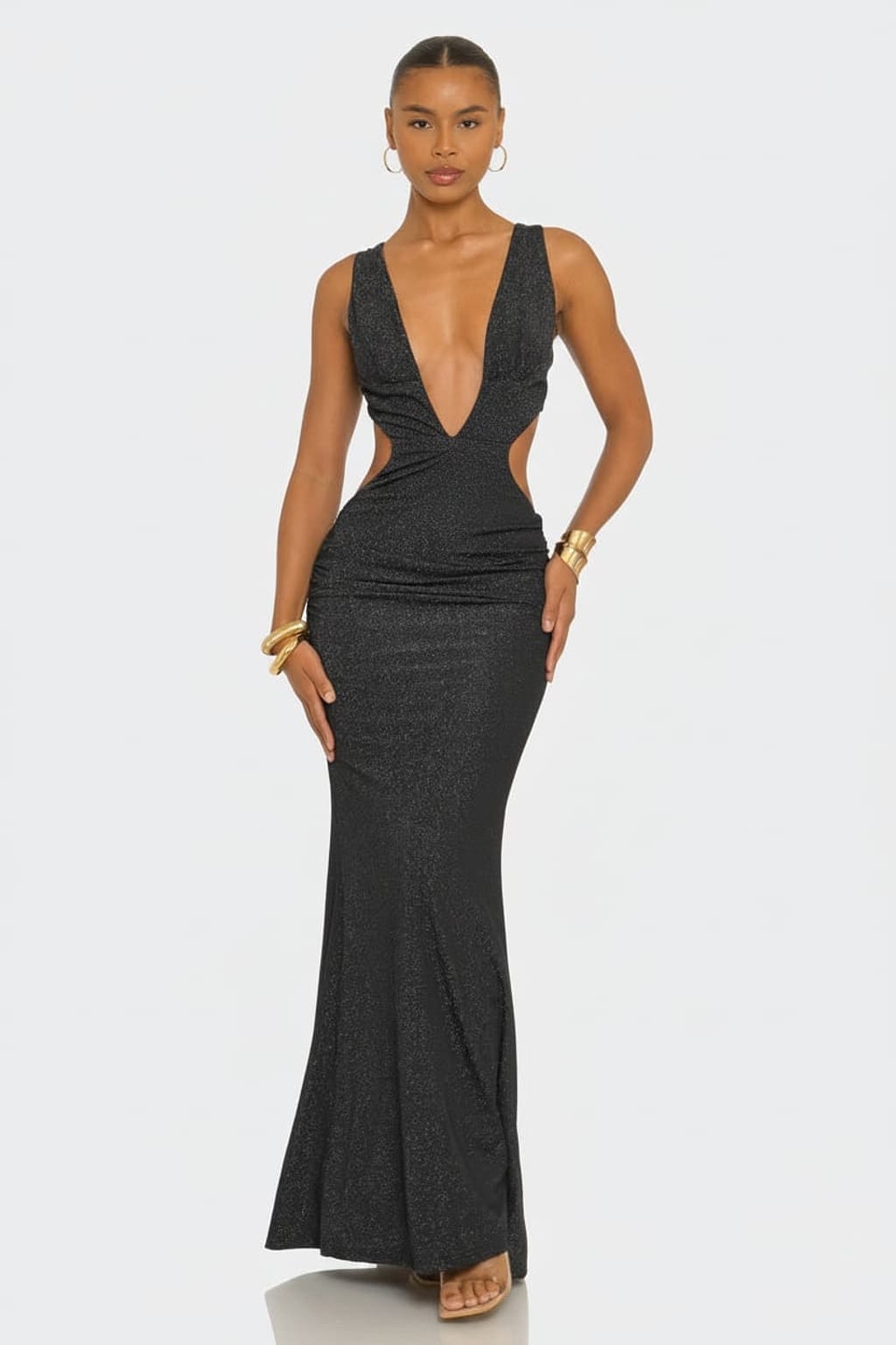 A woman modeling a dark charcoal gray sleeveless maxi dress with a plunging V-neckline, side cutouts, and a fitted mermaid silhouette against a light gray studio background.