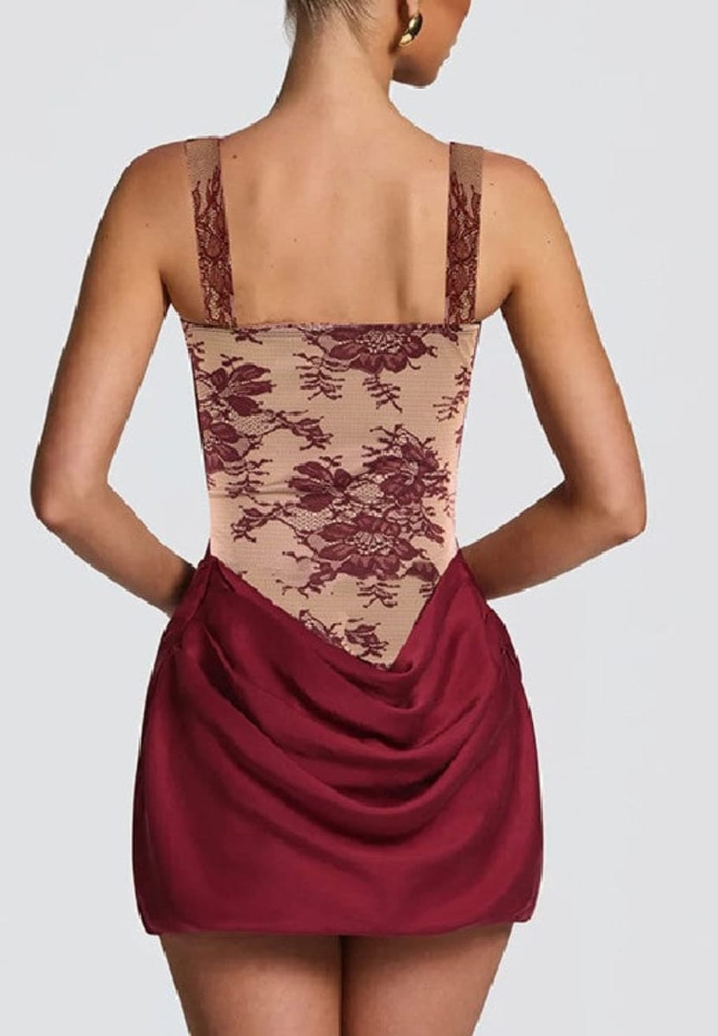 Rear view of a model wearing a short dress with a beige floral lace bodice and a draped burgundy skirt, set against a solid light gray background.