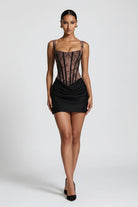 A model wearing a black and sheer brown lace mini dress with a corset-style bodice and ruched skirt, shown against a light gray studio background.