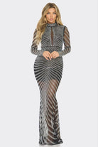 A woman modeling a long-sleeve, high-neck, floor-length gown covered in silver rhinestones over a sheer black mesh fabric, set against a plain light gray background.